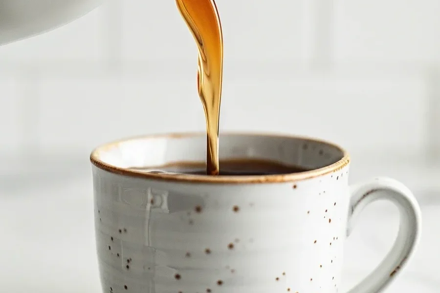 Homemade vanilla for skinny syrups being poured into a coffee cup on a white marble surface.